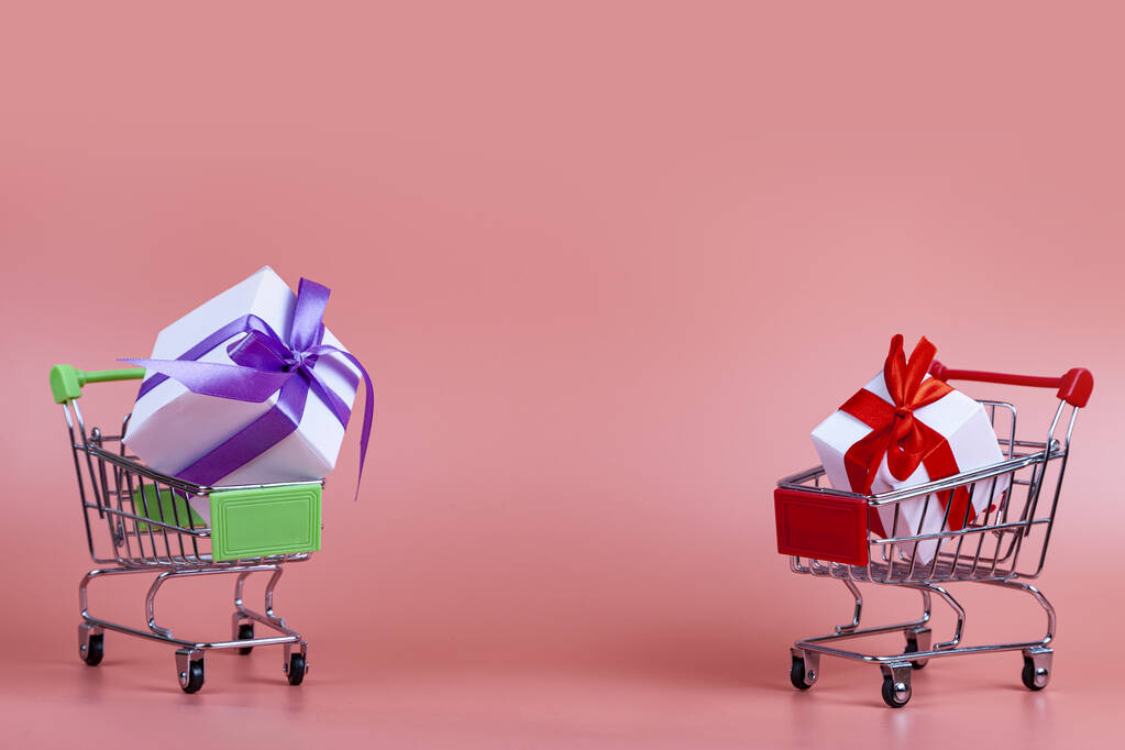 Carritos de compras y regalos sobre un fondo rosa. Concepto: comprar regalos. - Foto, Imagen