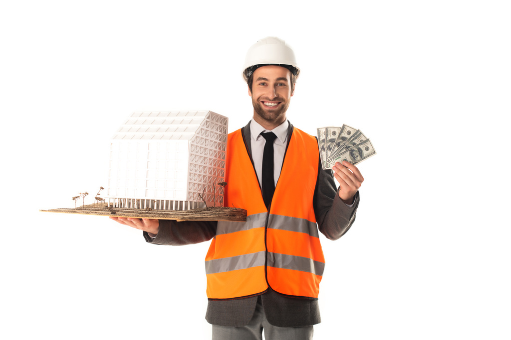 Engenheiro sorridente segurando modelo de construção e dólares isolados em branco  - Foto, Imagem