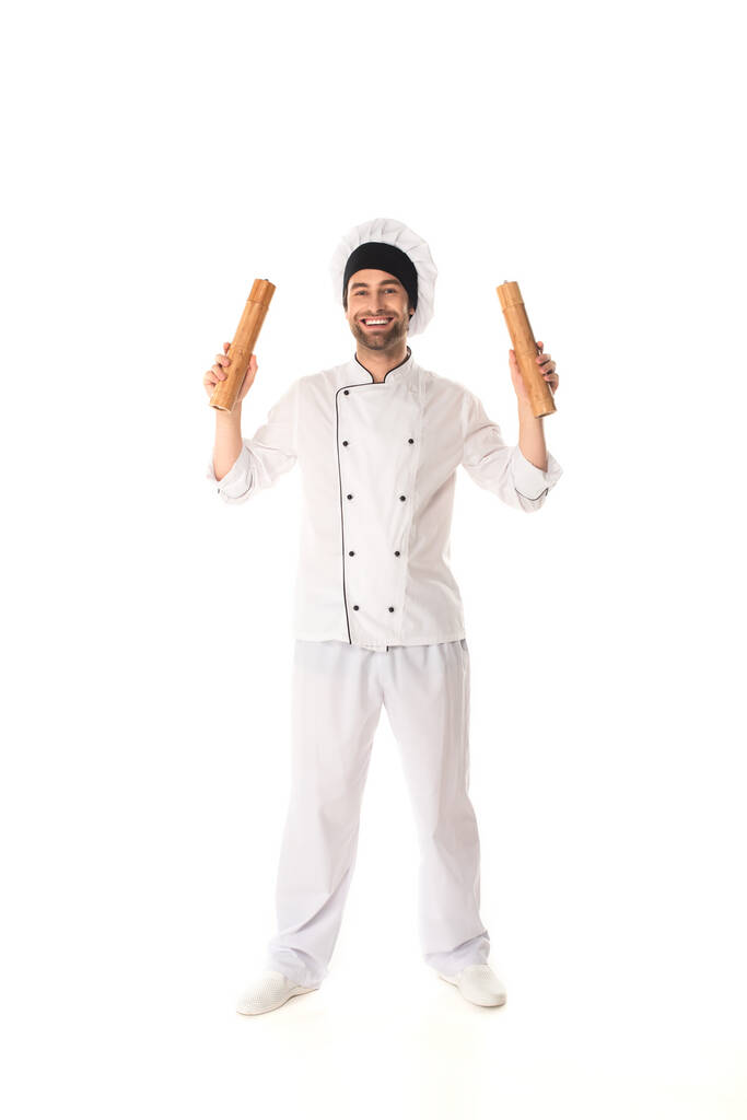 Полная длина улыбающийся шеф-повар держит перец и соль мельницы на белом фоне  - Фото, изображение