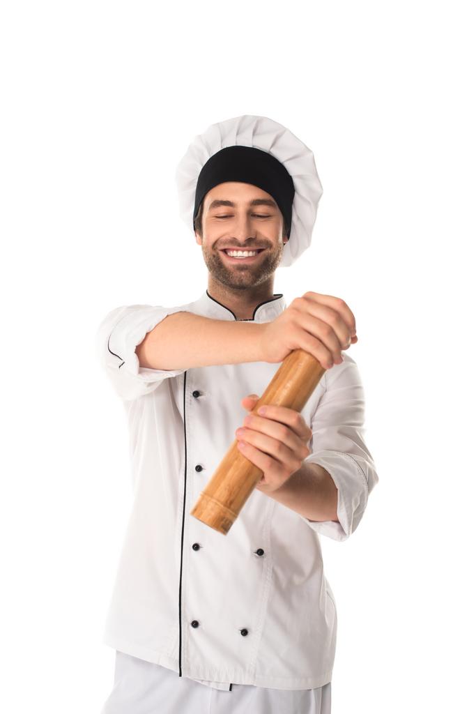 Улыбающийся шеф-повар держит перцовую мельницу изолированной на белом  - Фото, изображение