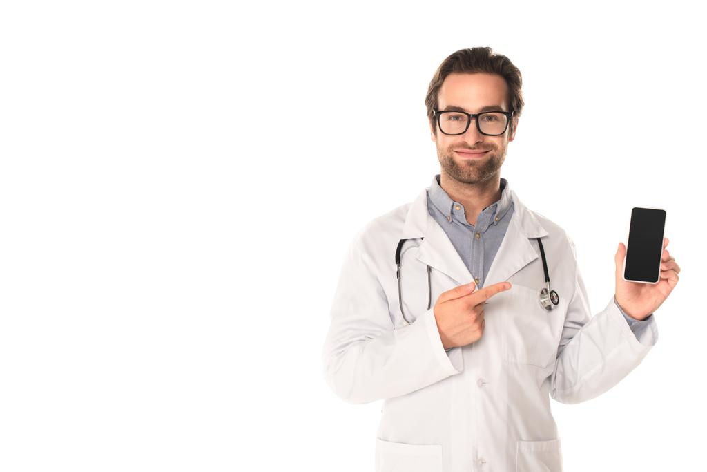 Smiling doctor pointing at smartphone isolated on white  - Photo, Image