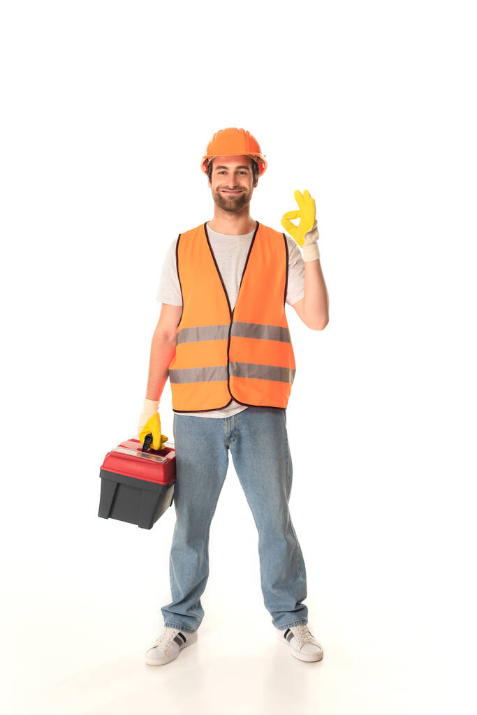 Réparateur souriant tenant la boîte à outils et montrant ok sur fond blanc  - Photo, image