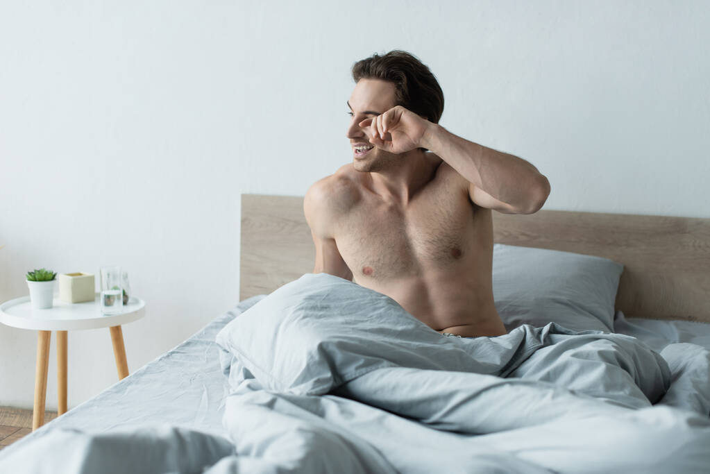 awake man smiling and rubbing eye on bed in morning - Photo, Image