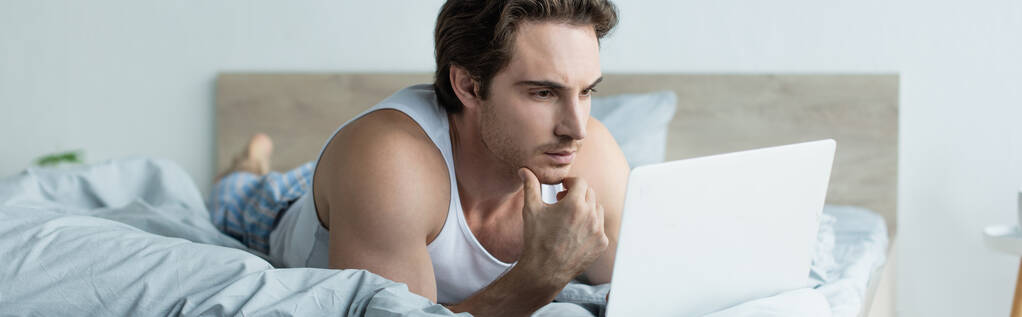вдумчивый человек, глядя на ноутбук, лежа в постели, баннер - Фото, изображение