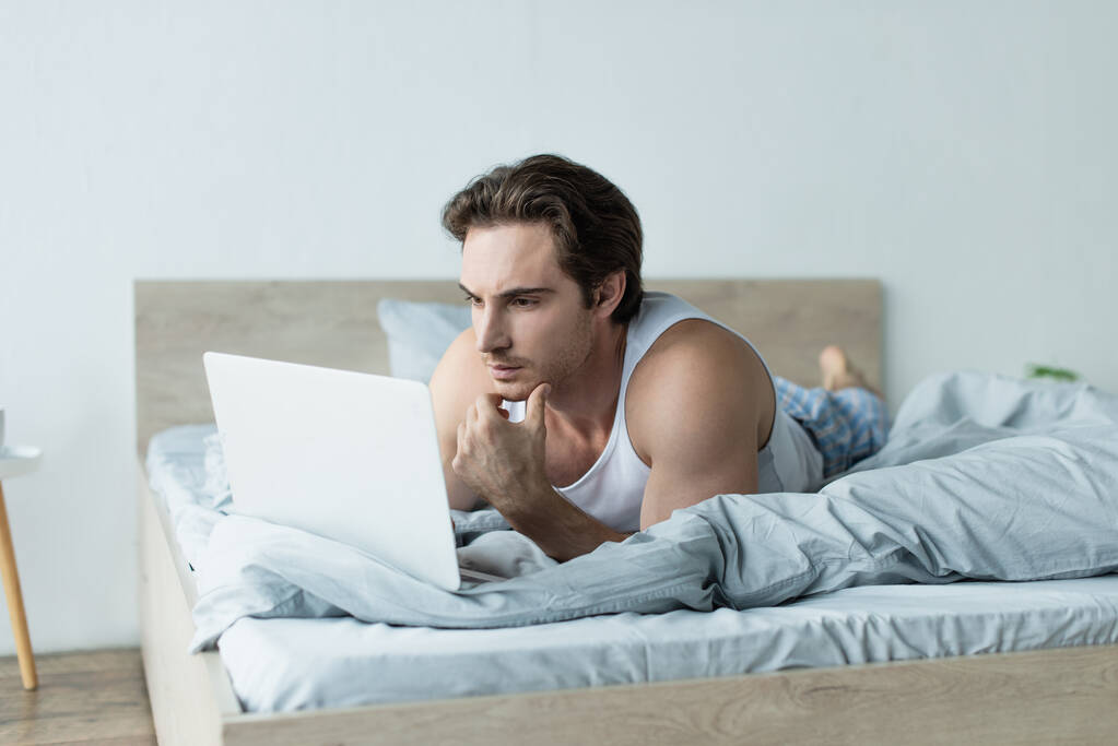 young man thinking while using laptop in bed - Photo, Image