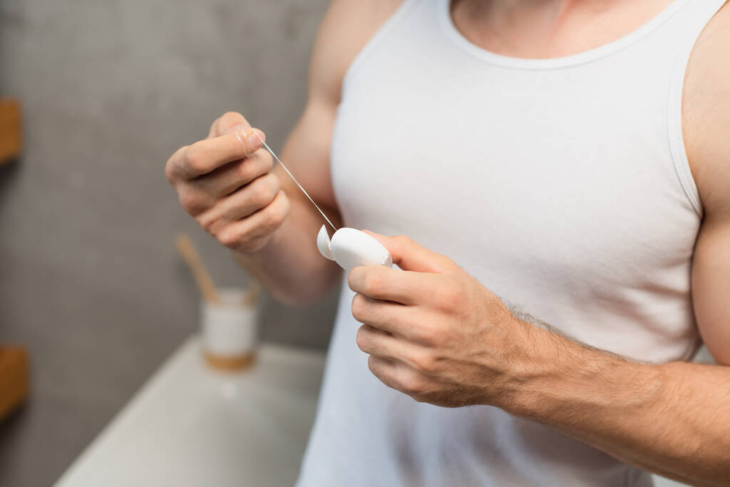 partial view of man in white tank top holding dental floss in bathroom - Photo, Image