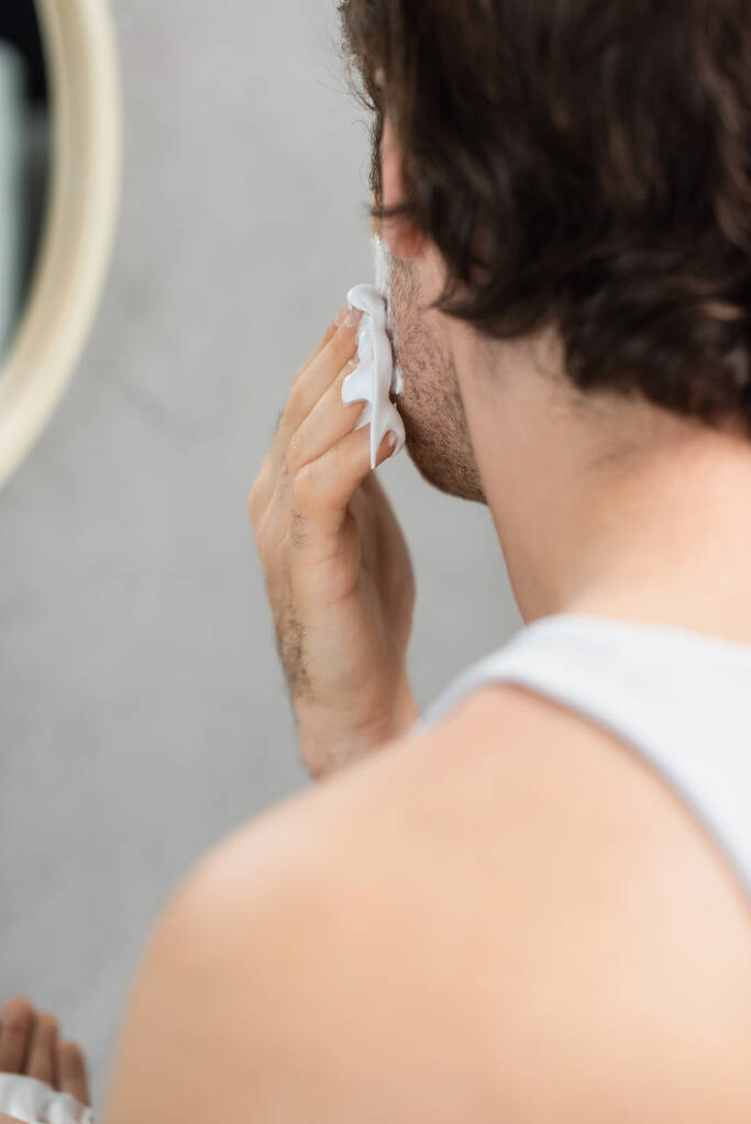 vista parcial del hombre borroso aplicando espuma de afeitar en la cara  - Foto, Imagen
