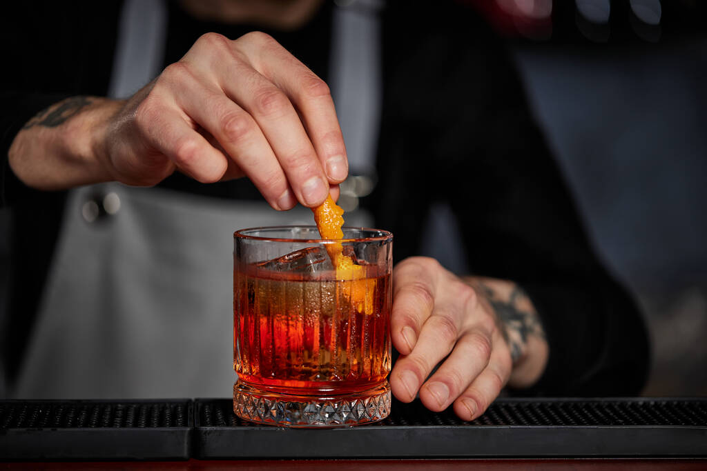 бармен делает коктейль в стакане с апельсиновой кожурой - Фото, изображение