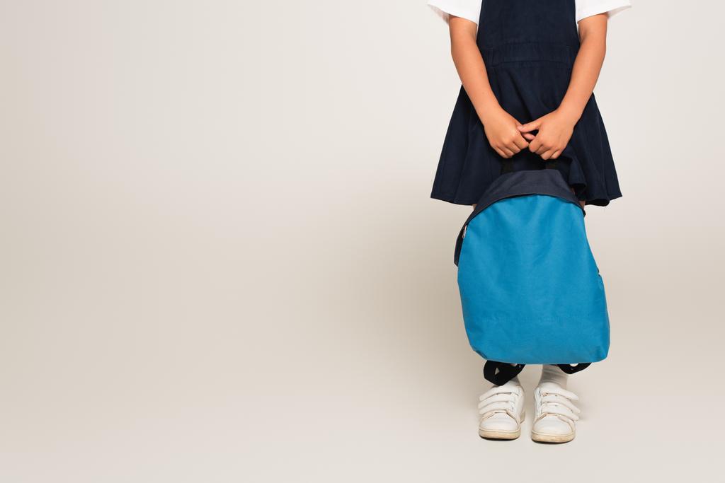 bijgesneden weergave van schoolmeisje staan met blauwe rugzak op grijs - Foto, afbeelding