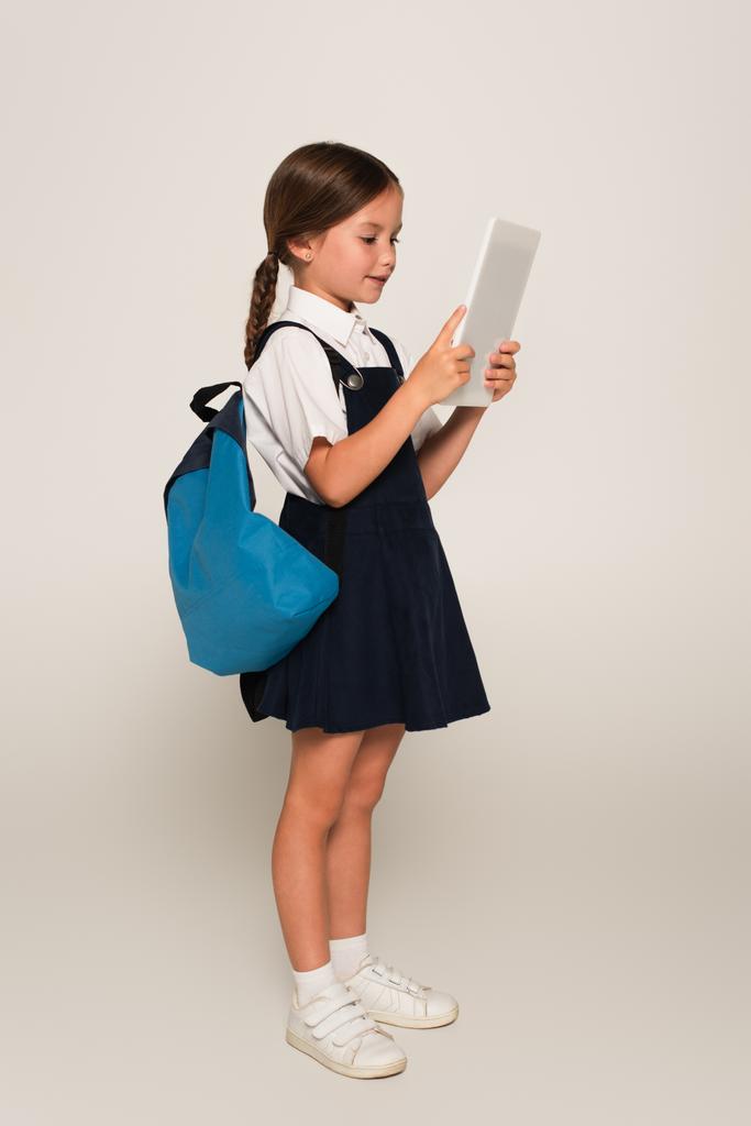 Schulmädchen mit blauem Rucksack mit digitalem Tablet auf grau - Foto, Bild