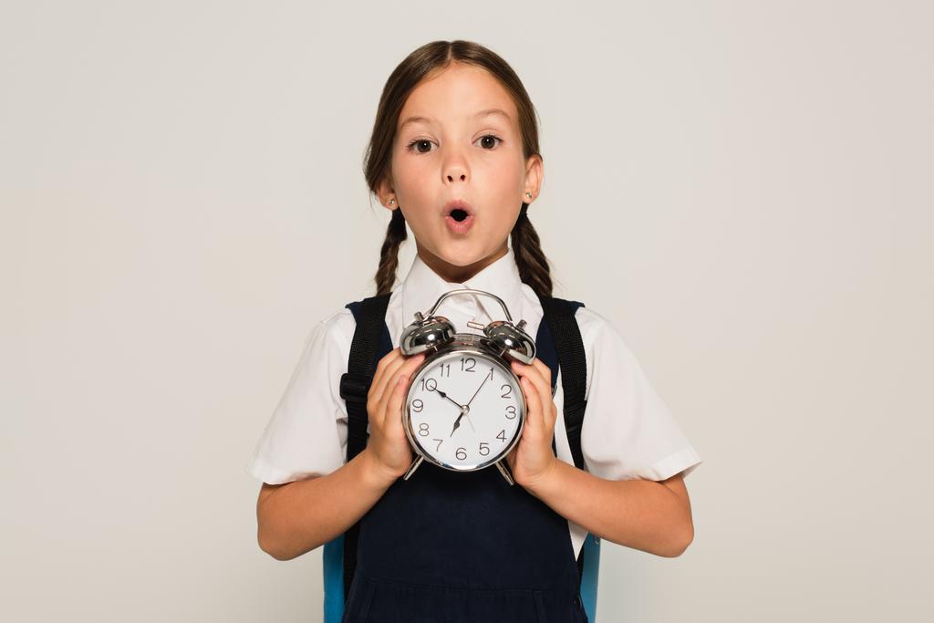 astonished schoolkid showing large alarm clock isolated on grey - Photo, Image