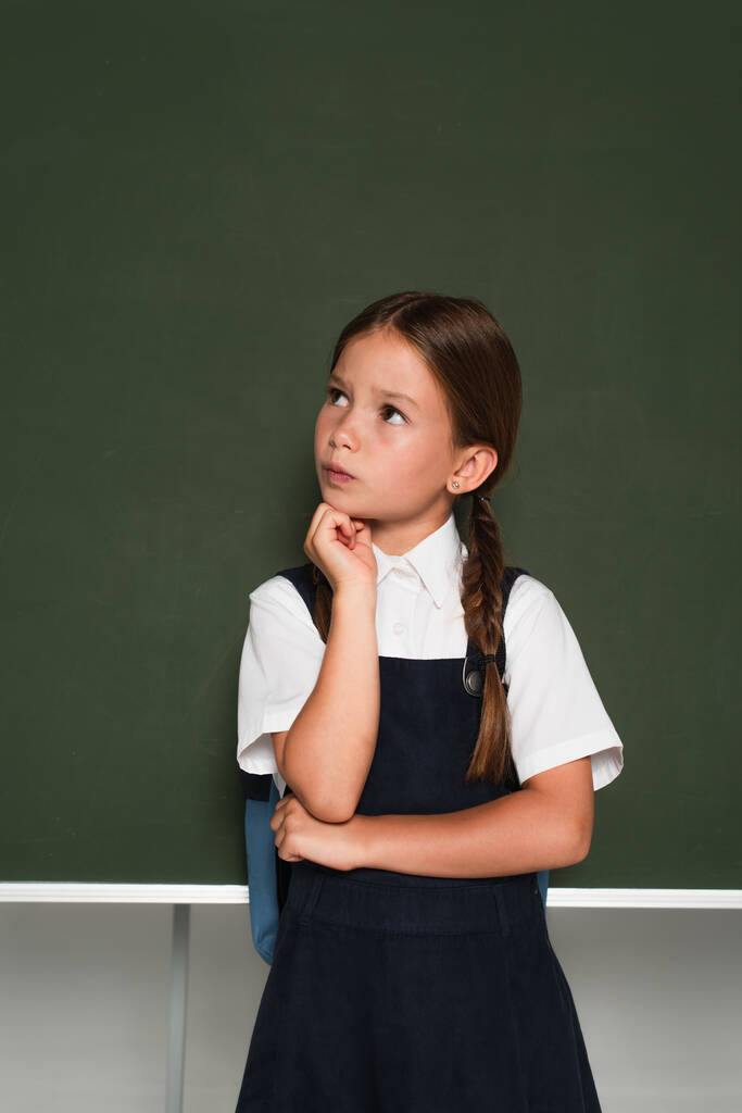 huomaavainen koulupoika katselee pois ja pitää kädestä lähellä kasvoja seisoessaan liitutaulu harmaa - Valokuva, kuva