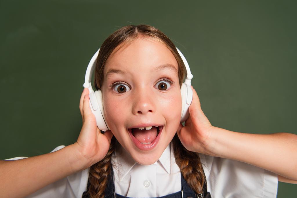 estudante animado com boca aberta tocando fones de ouvido enquanto estava perto de quadro-negro - Foto, Imagem