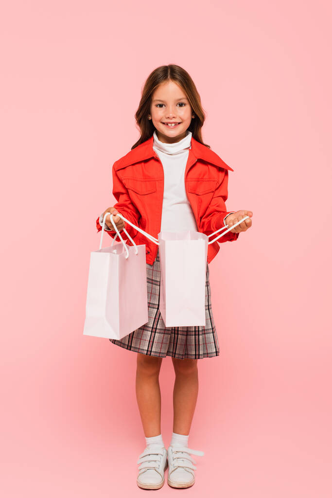 bambino alla moda sorridente alla fotocamera mentre apriva la borsa della spesa sul rosa - Foto, immagini