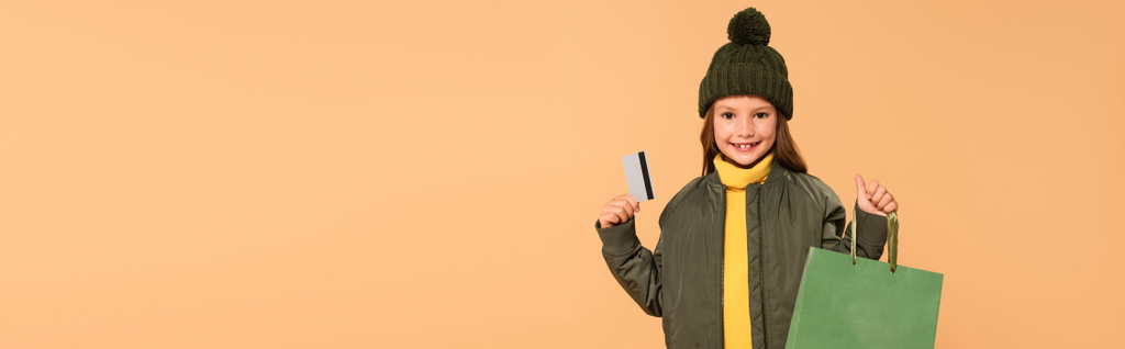 счастливая и стильная девушка с сумкой и кредитной карты изолированы на бежевый, баннер - Фото, изображение