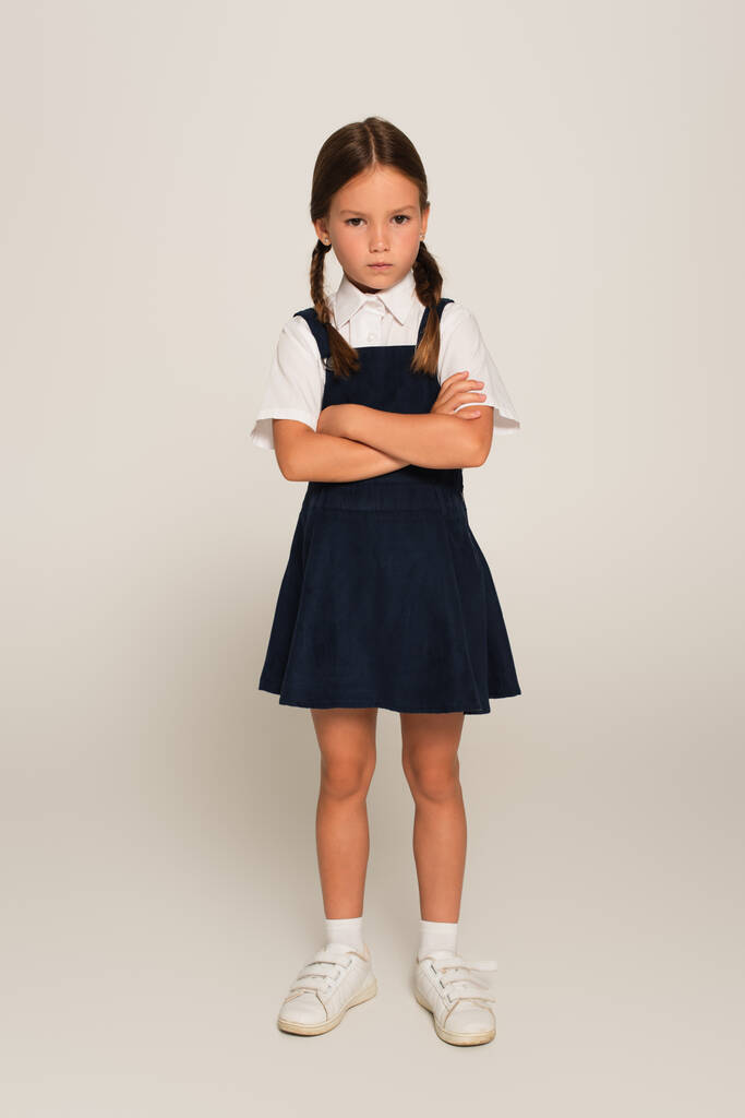 täyspitkä näkymä loukkaantuneesta koululaisesta seisomassa ristissä kädet harmaalla - Valokuva, kuva