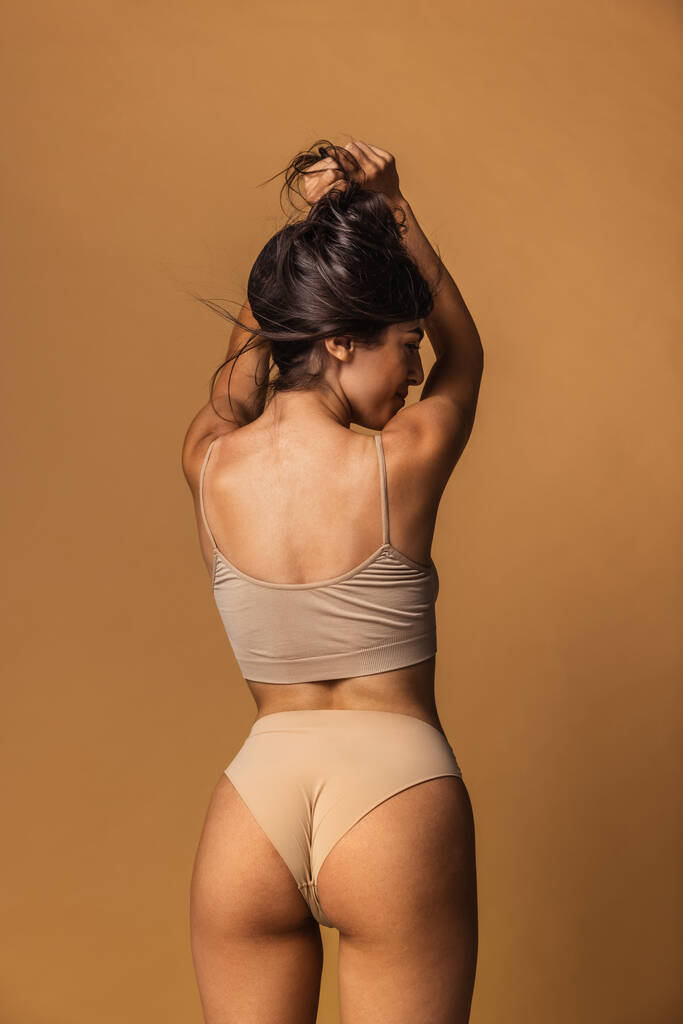 Achteraanzicht van sportief lichaam van jonge blanke vrouw geïsoleerd op bruine studioachtergrond. Natuurlijke schoonheid concept - Foto, afbeelding