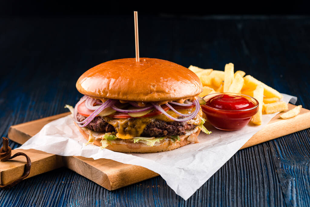 Zblízka gurmánský hamburger se slaninou na dřevěném stole, velký burger s bramborami a kečupem, velký burger a hranolky - Fotografie, Obrázek