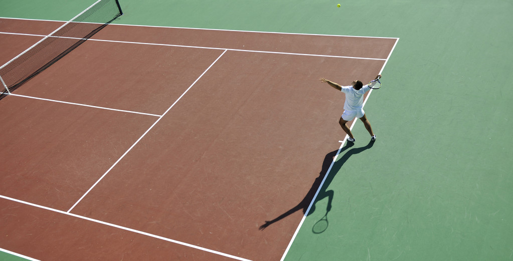 Joven jugar al tenis al aire libre en el campo de tenis naranja en la mañana temprano
 - Foto, Imagen