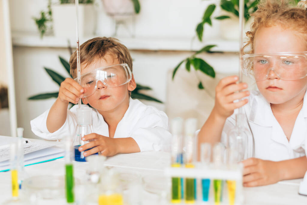 Σοβαρό μικρό αγόρι και κορίτσι με άσπρες στολές που διεξάγουν χημικά πειράματα σε ένα εργαστήριο.Επιστροφή στην σχολική έννοια.Νέοι επιστήμονες.Φυσικές επιστήμες.Προσχολική και σχολική εκπαίδευση των παιδιών. - Φωτογραφία, εικόνα