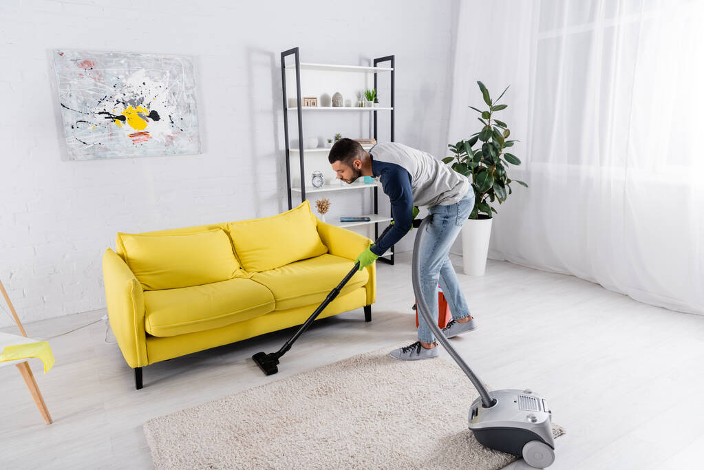 Вид збоку людини прибирання підлоги з пилососом в домашніх умовах
  - Фото, зображення