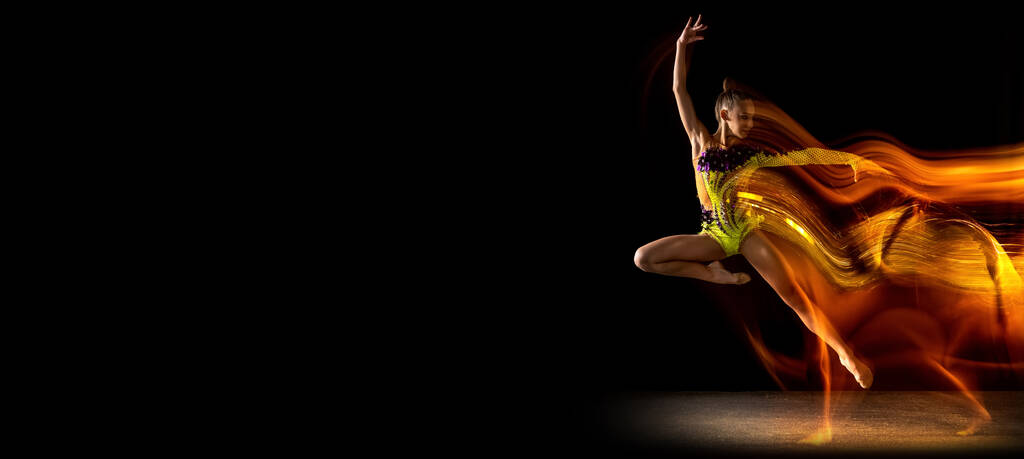 Volador. Retrato de niña, artista de gimnasia rítmica en acción aislado sobre fondo de estudio oscuro con luz mixta. Concepto de deporte, acción, aspiración, belleza - Foto, imagen