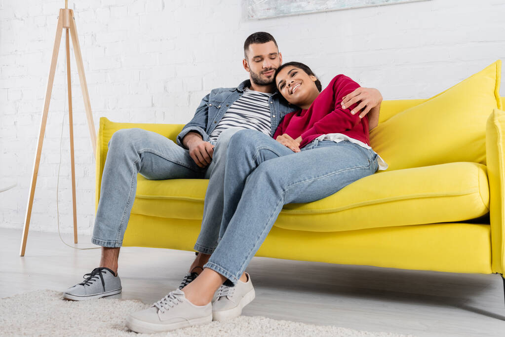 Young man hugging african american girlfriend on couch  - Photo, Image