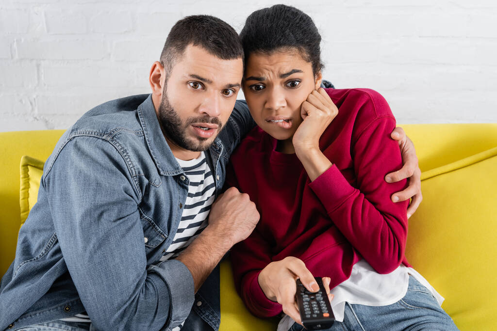 Homme effrayé étreignant petite amie afro-américaine avec télécommande  - Photo, image