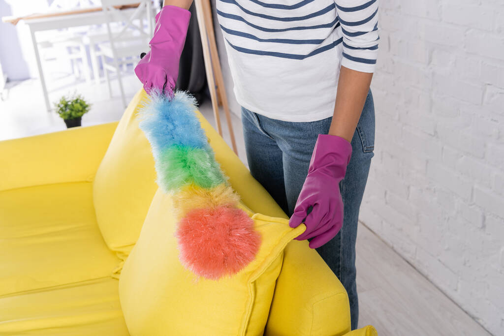 Обрізаний вид жінки в гумових рукавичках чистить диван з пиловим пензлем
  - Фото, зображення