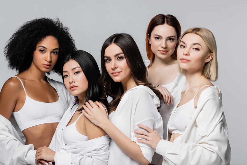 modelos americanos asiáticos y africanos en camisas blancas posando con mujeres jóvenes aisladas en gris - Foto, Imagen