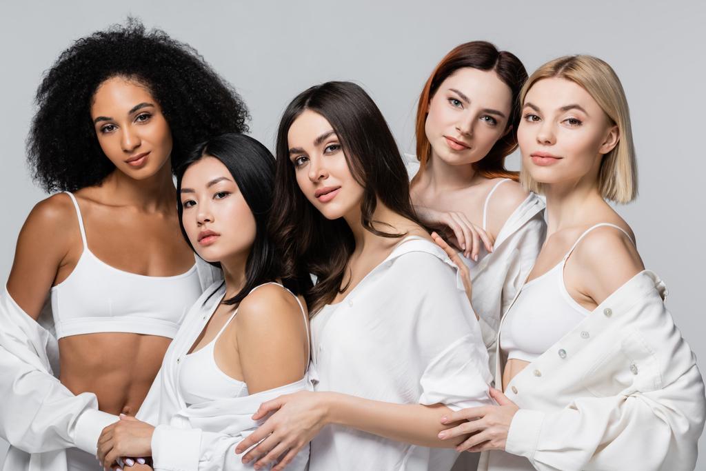 morena asiático y africano americano modelos en blanco camisas posando con jóvenes mujeres aislado en gris - Foto, Imagen