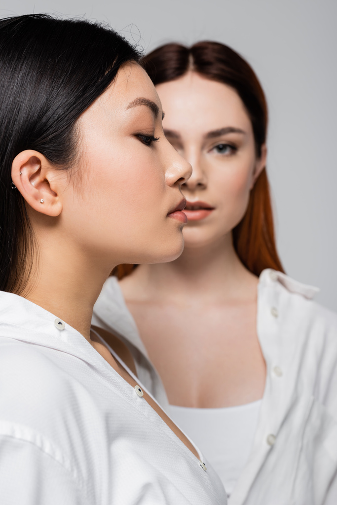 profil azjatycki model pozowanie w pobliżu rozmyty ruda kobieta odizolowany na szary - Zdjęcie, obraz