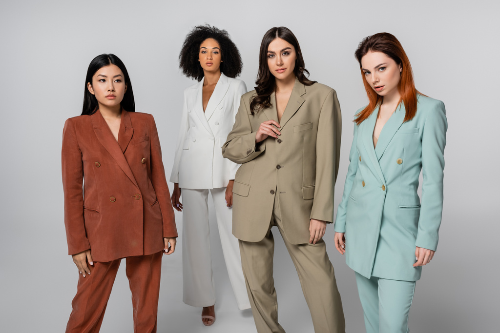 multiethnische Gruppe von Models in pastellfarbenen Anzügen posiert auf grau - Foto, Bild