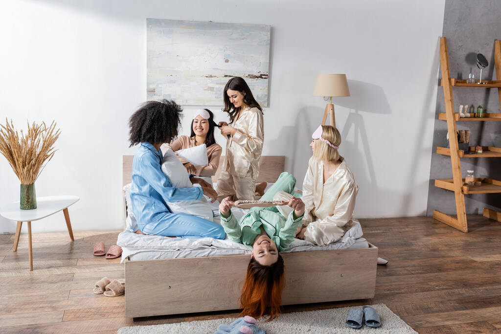 ryhmä iloisia rotujenvälinen ystäviä pyjamassa istuu sängyllä pyjamabileiden aikana  - Valokuva, kuva