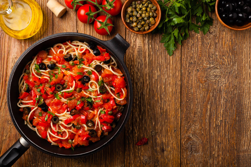 Italienische Spaghetti alla Pultanesca mit Tomaten und Oliven. Serviert ohne Fleisch und Käse. Ansicht von oben. Natürlicher hölzerner Hintergrund.  - Foto, Bild