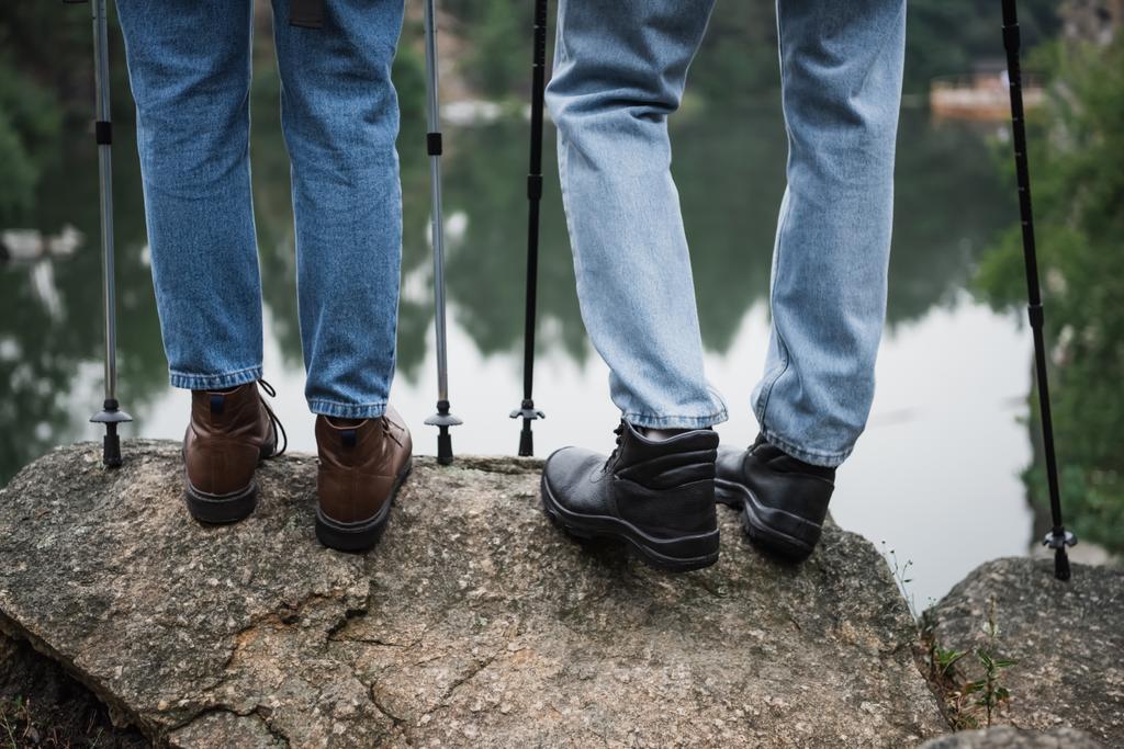 vista parcial de pareja joven de pie con bastones de senderismo en la roca - Foto, imagen