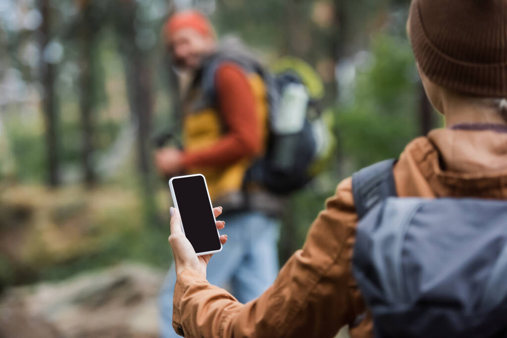 nő gazdaság smartphone míg üres képernyő közelében elmosódott férfi erdőben  - Fotó, kép