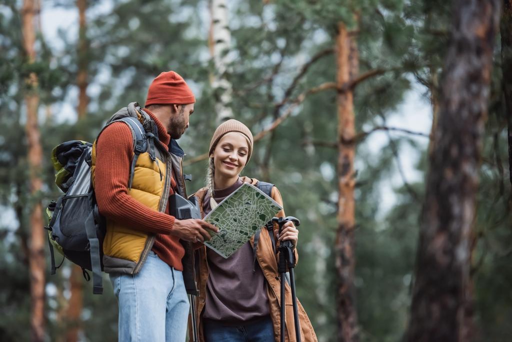 man holding map and looking at cheerful woman with hiking sticks - Φωτογραφία, εικόνα