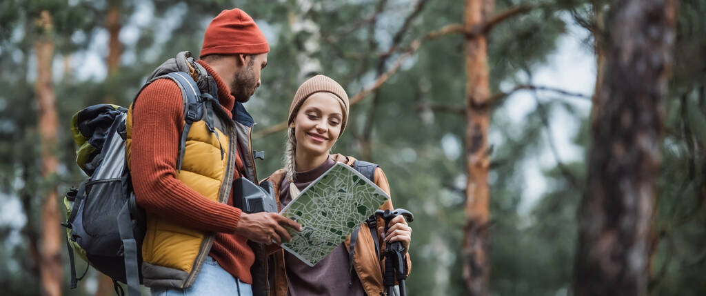 muž drží mapu a dívá se na veselou ženu s turistickými holemi, prapor - Fotografie, Obrázek
