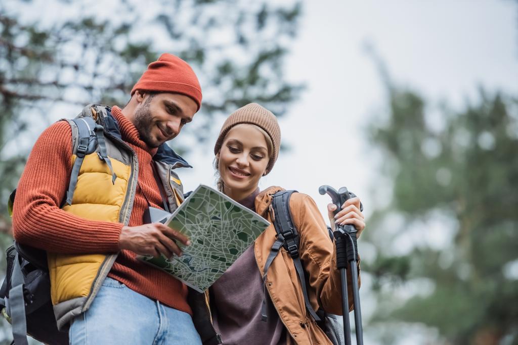 nízký úhel pohledu na šťastný pár v klobouky při pohledu na mapu v lese - Fotografie, Obrázek