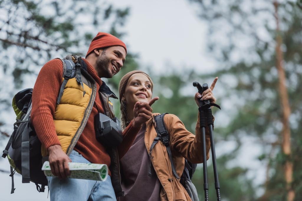niski kąt widzenia szczęśliwy mężczyzna i kobieta wskazując palcami w lesie  - Zdjęcie, obraz