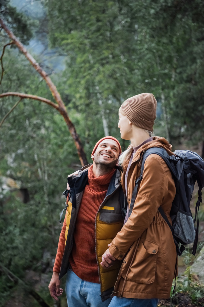 pareja joven y feliz tomados de la mano mientras se miran en el bosque  - Foto, imagen