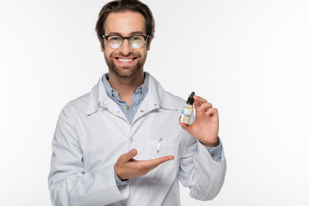 medico felice indicando fiala con olio di canapa isolato su bianco - Foto, immagini