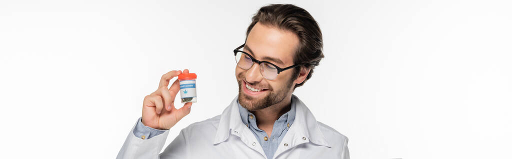 szczęśliwy lekarz patrząc na pojemnik z marihuany medycznej izolowane na białym, baner - Zdjęcie, obraz