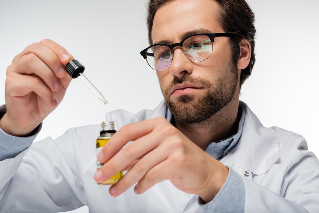 врач в очках держит капельницу и бутылку масла cbd изолированы на белом - Фото, изображение