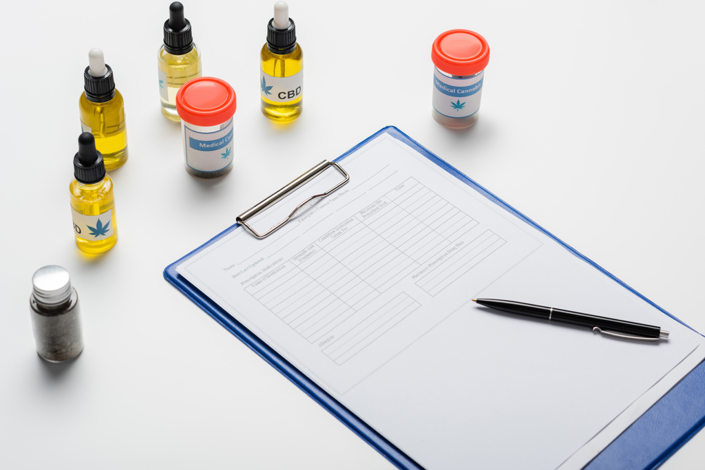 Flaschen und Behälter mit medizinischem Cannabis in Rezeptnähe auf weißem Schreibtisch - Foto, Bild