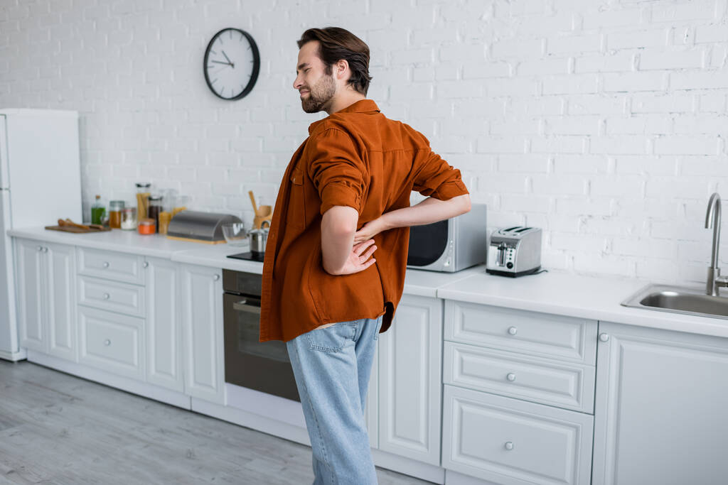 férfi megérinti vissza, miközben szenved a fájdalom a konyhában - Fotó, kép