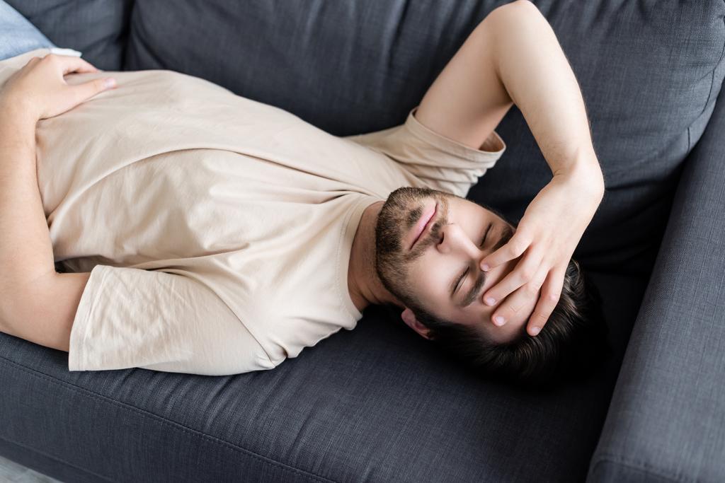 Άρρωστος άντρας με κλειστά μάτια ξαπλωμένος στον καναπέ στο σπίτι  - Φωτογραφία, εικόνα