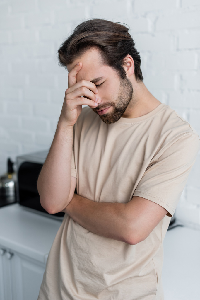 Homem doente com olho fechado em pé na cozinha  - Foto, Imagem