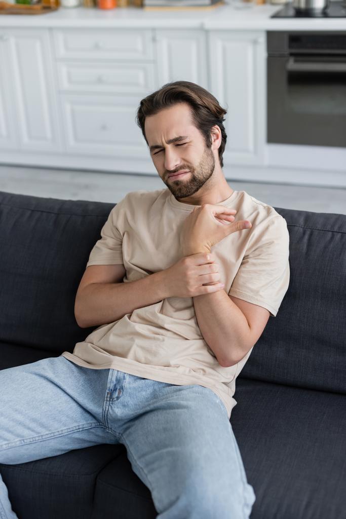 Hombre tocando el brazo mientras siente dolor en casa  - Foto, Imagen